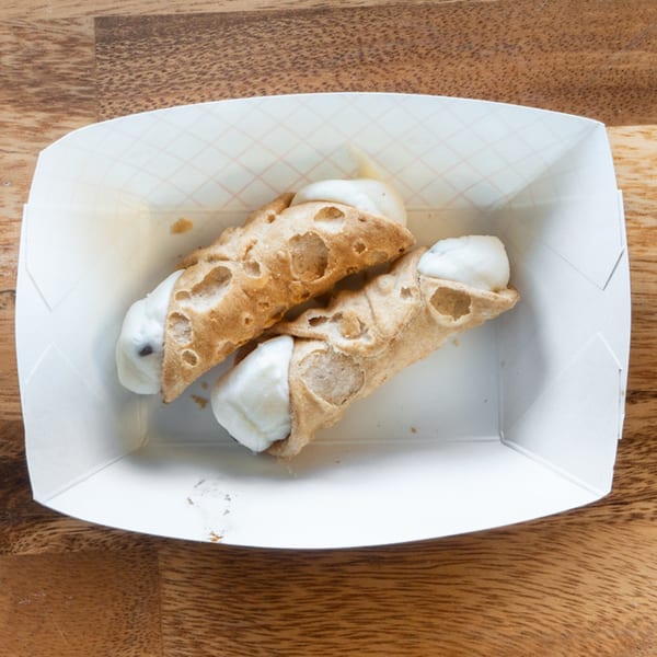 Two cannolis with white cream filling in a white paper tray on a wooden table.