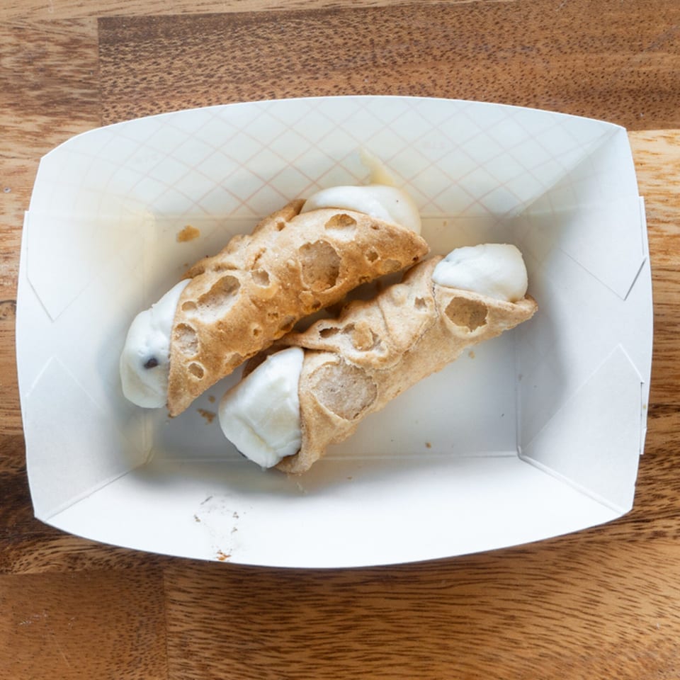 Two cannolis with white cream filling in a white paper tray on a wooden table.