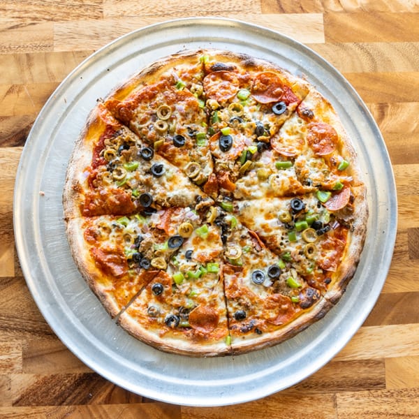 A whole Solar Slice Pizza, cut into slices, with pepperoni, olives, and green peppers.