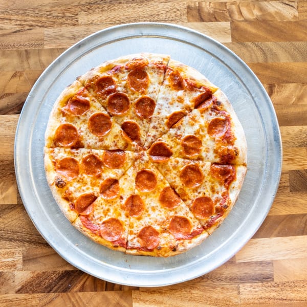 A whole pepperoni pizza, cut into slices, on a silver pizza pan atop a wooden table.