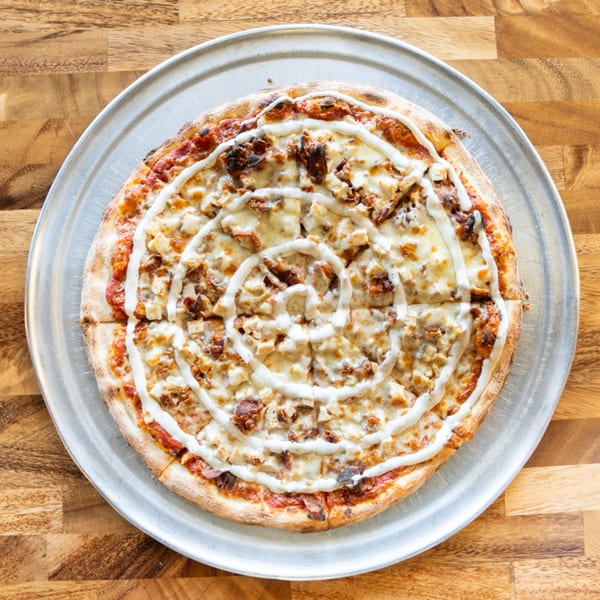 Top-down view of a Solar Slice Pizza with chicken, cheese, and a spiral of white sauce.