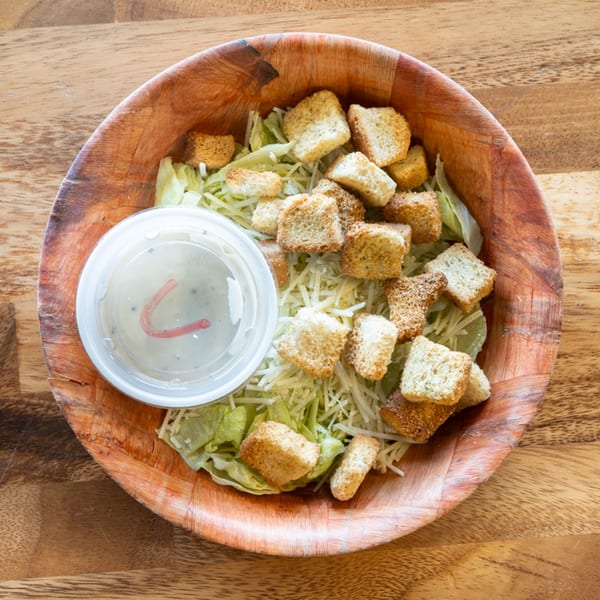 Caesar salad with croutons and a side of dressing in a wooden bowl on a wooden table.